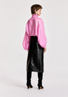 A model is shown from the back wearing a vibrant pink long-sleeve blouse with voluminous balloon sleeves, a black faux-leather midi skirt, black leggings, and black high-heeled shoes, set against a plain light gray studio background.