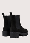 A pair of black Chelsea boots with chunky lug soles and elastic side panels, shown from a rear three-quarter angle on a light beige background.