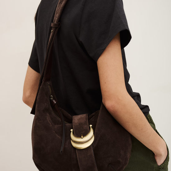 Person wearing a brown suede bag over one shoulder on a plain background