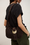 Person wearing a brown suede bag over one shoulder on a plain background