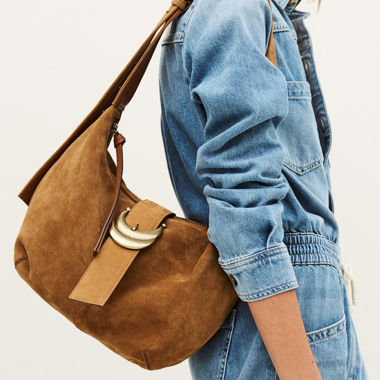 Person wearing a denim jacket with a brown leather handbag on a plain background