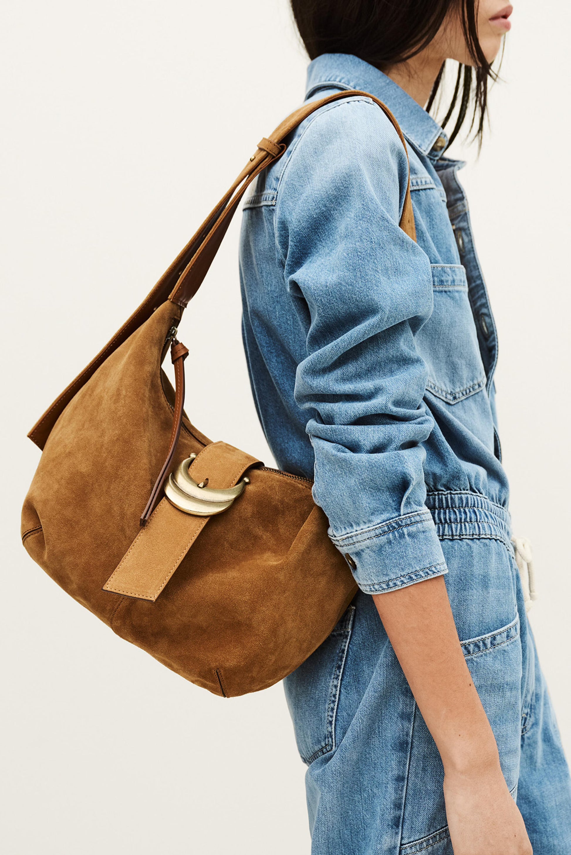 Person wearing a denim jacket with a brown leather handbag on a plain background