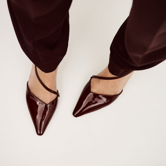 Red patent shoes with pointed toes worn with matching pants on a light background