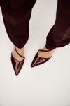 Red patent shoes with pointed toes worn with matching pants on a light background
