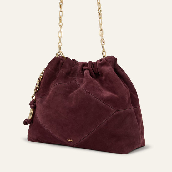 A burgundy suede bucket bag with a gold chain shoulder strap, shown on a light cream background.