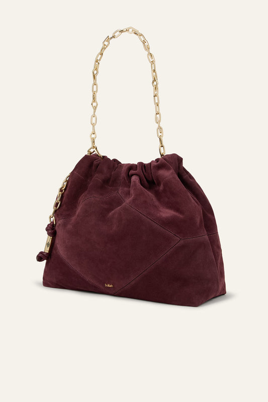 A burgundy suede bucket bag with a gold chain shoulder strap, shown on a light cream background.