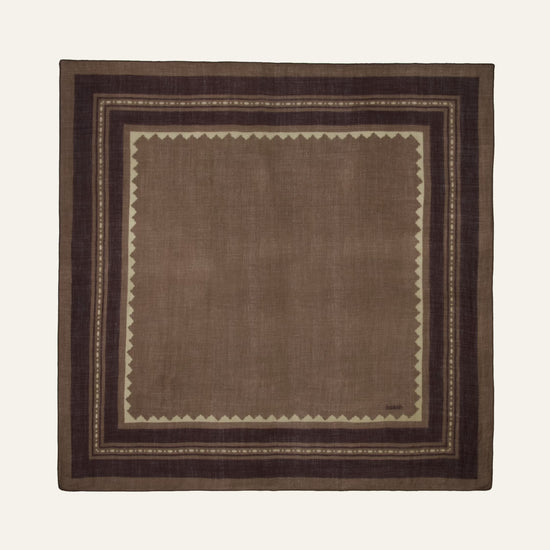 A square brown woven textile with a geometric border pattern, displayed flat against a light cream background.