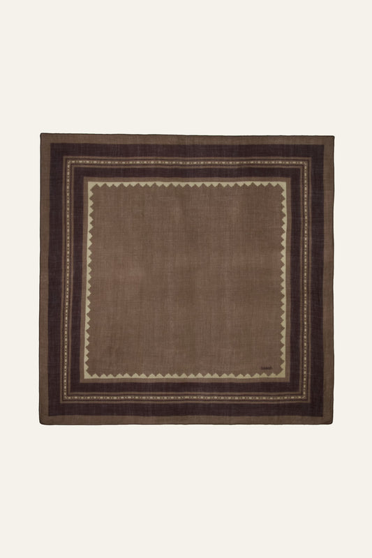 A square brown woven textile with a geometric border pattern, displayed flat against a light cream background.