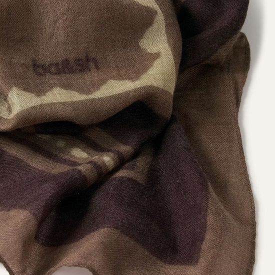 A close-up of a draped scarf in a brown, beige, and dark plum camouflage pattern, featuring the embroidered brand name 'balenciaga' on the left side.