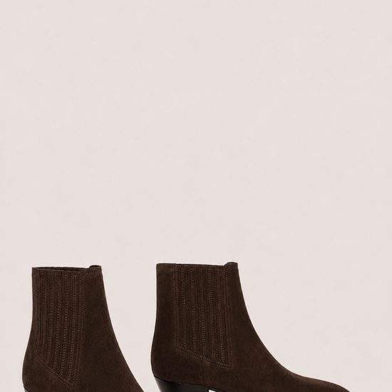 A pair of dark brown suede ankle boots with ribbed elastic side panels and low block heels, displayed against a solid light beige background.