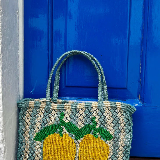 Blue and beige stripe bag with lemons leaning against a blue door