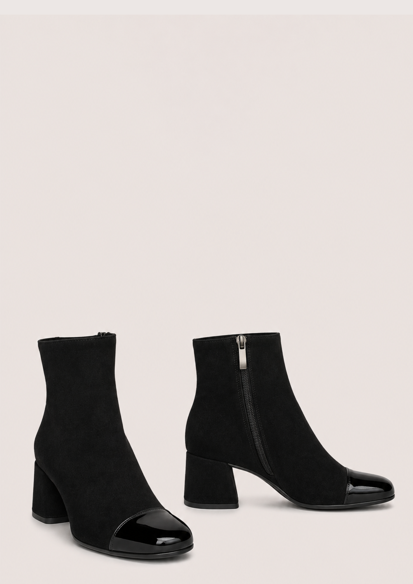 A pair of black ankle boots with a block heel and glossy patent leather toe caps, shown against a solid light beige background.