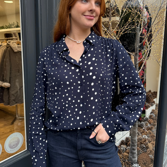 Navy long sleeved shirt with different sized white dots, styled with dark denim.