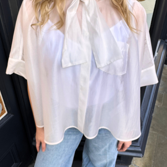 Person wearing a white blouse with a bow tie and light blue jeans.