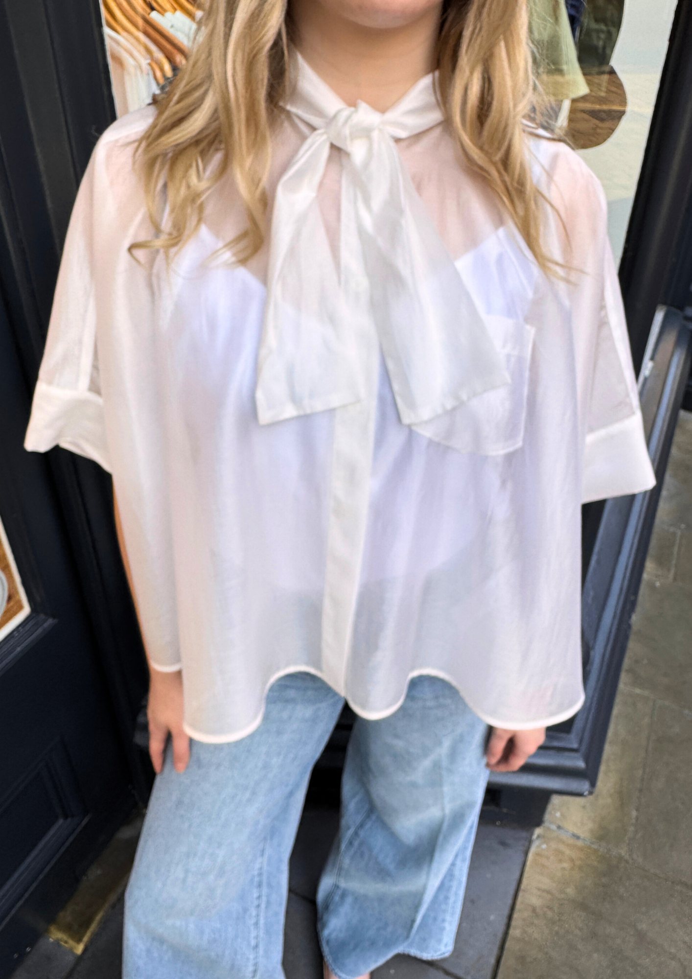 Person wearing a white blouse with a bow tie and light blue jeans.