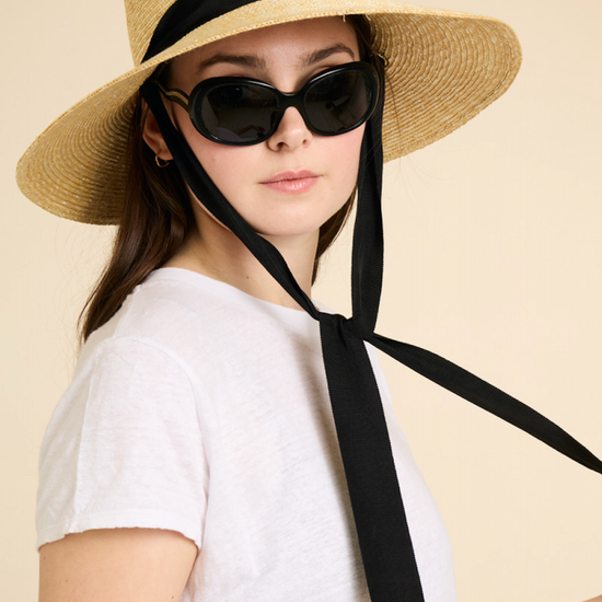 Person wearing a straw hat with a black ribbon and sunglasses on a beige background