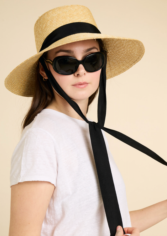 Person wearing a straw hat with a black ribbon and sunglasses on a beige background