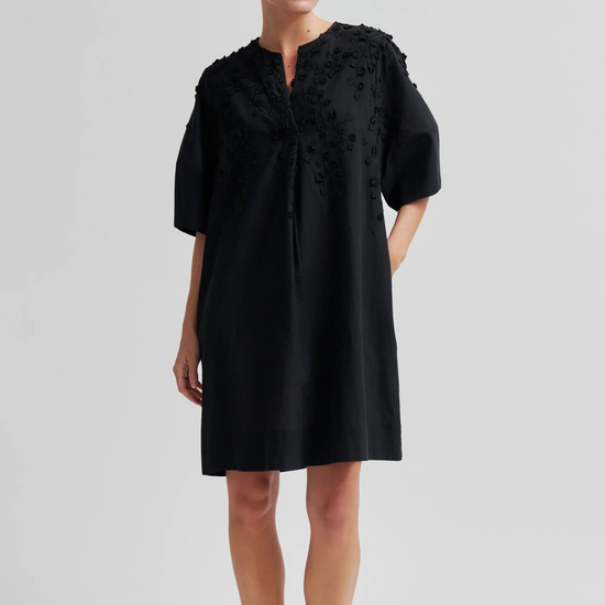 Woman wearing a black dress with floral details on a light gray background