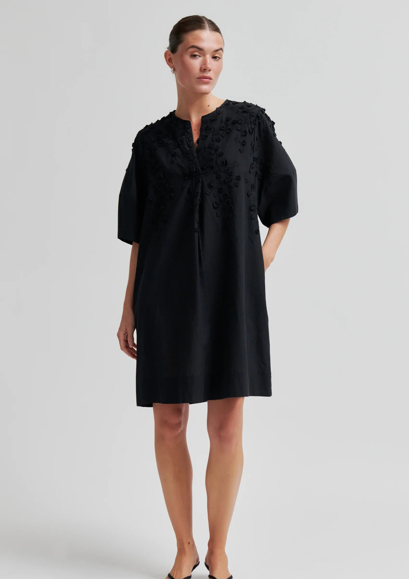 Woman wearing a black dress with floral details on a light gray background