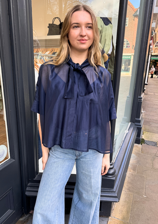 Woman wearing a navy blouse with a tie detail and light blue jeans.