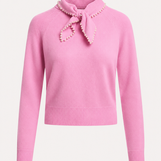 A pink knit sweater with a high folded collar, a matching bow at the neck, and a border of small pearl-like embellishments. The sweater has long sleeves with ribbed cuffs and a ribbed hem, shown against a plain light background.