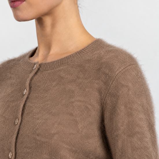 Close-up of a model wearing a fuzzy taupe-brown knit cardigan sweater with a buttoned front.