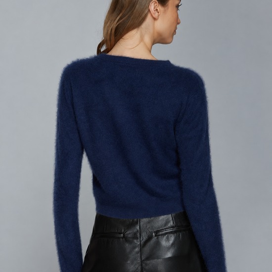 A woman shown from the back wearing a fuzzy navy blue long-sleeve sweater and black leather pants against a plain gray studio background.