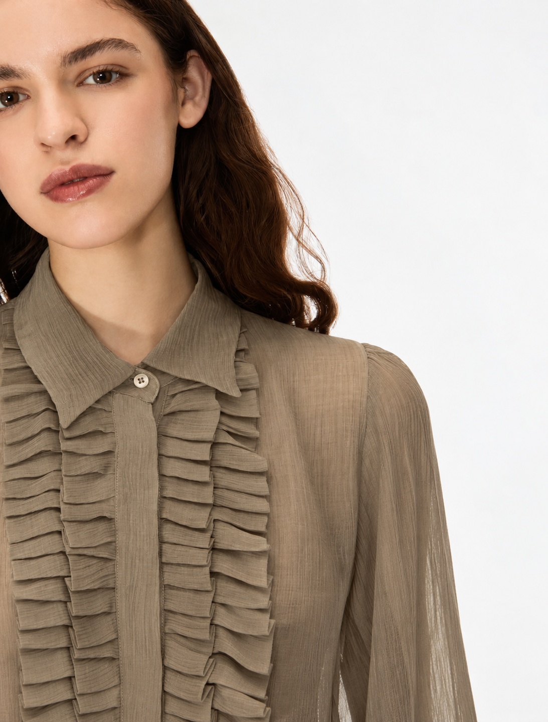 A close-up of a model wearing a taupe brown ruffled blouse with a pointed collar and a single button, set against a plain white background.