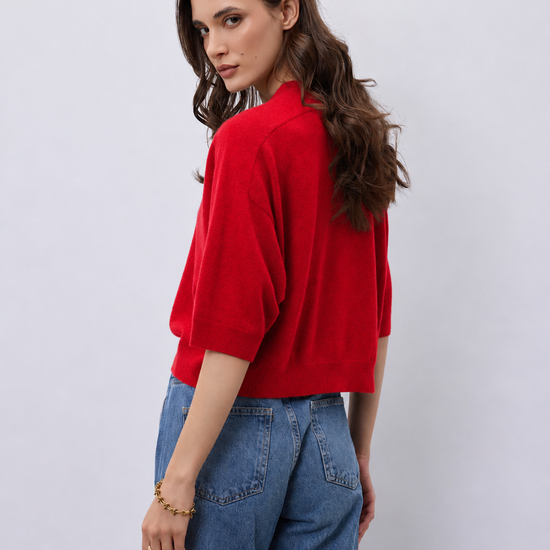 Model wearing a bright red cashmere mid length sleeve knit, with blue jeans on a white background