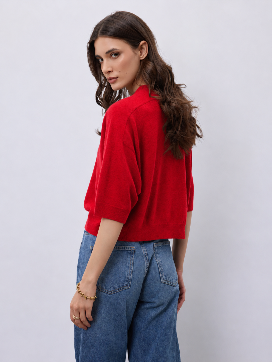 Model wearing a bright red cashmere mid length sleeve knit, with blue jeans on a white background