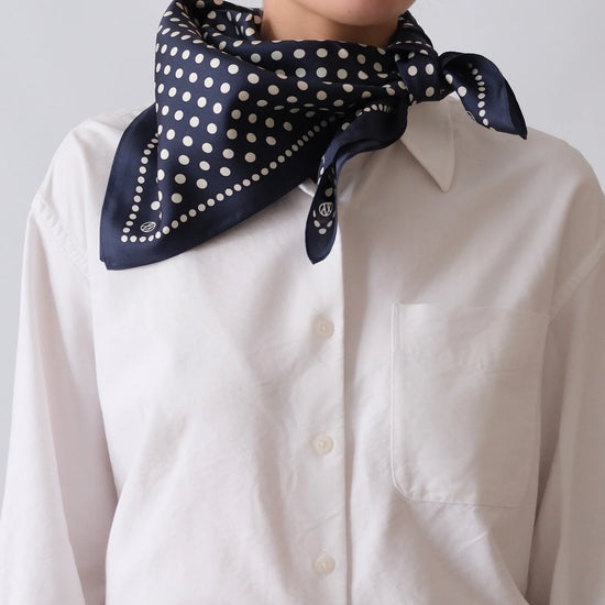 Person wearing a navy blue scarf with white polka dots over a white shirt against a light gray background