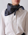 Person wearing a navy blue scarf with white polka dots over a white shirt against a light gray background