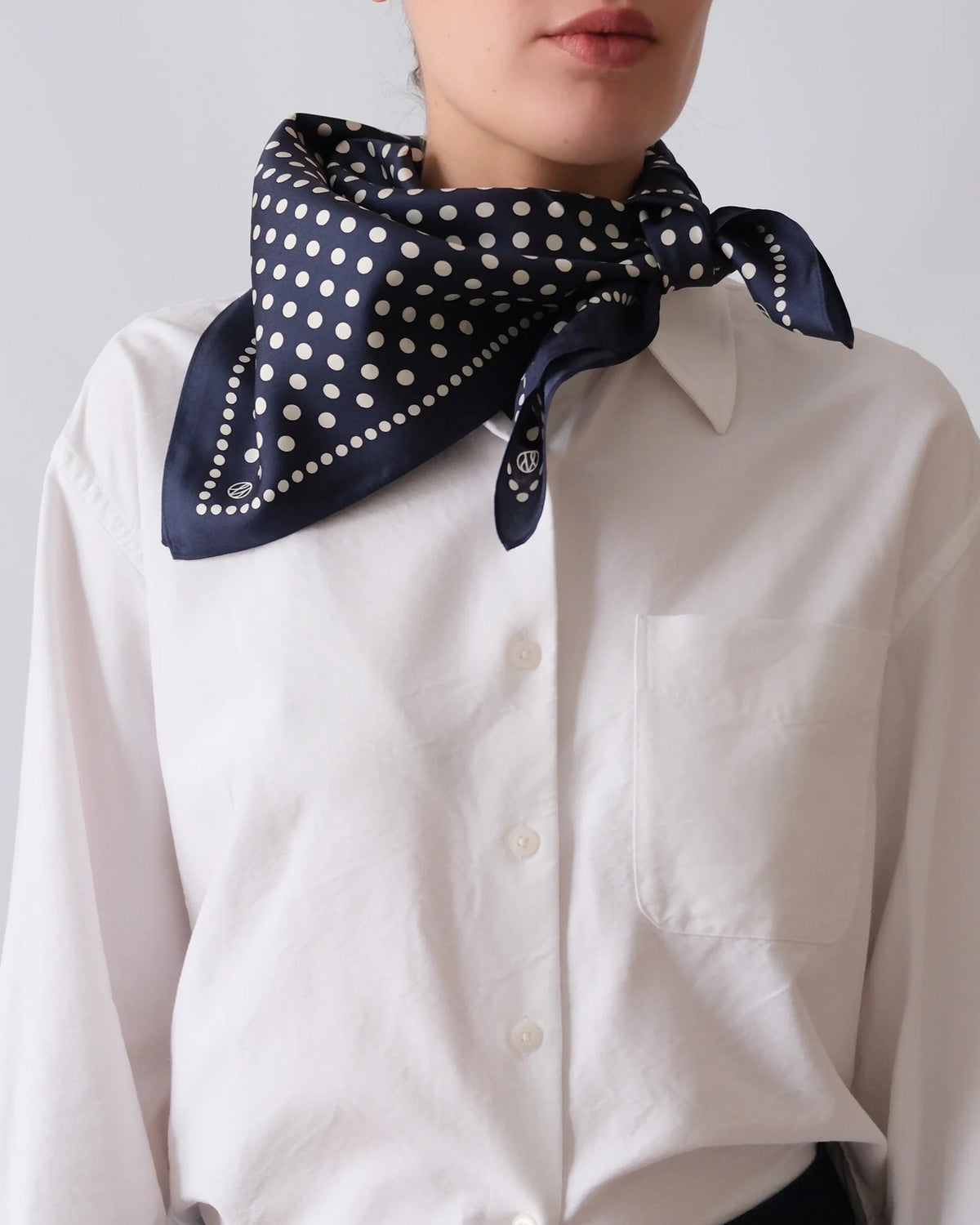 Person wearing a navy blue scarf with white polka dots over a white shirt against a light gray background