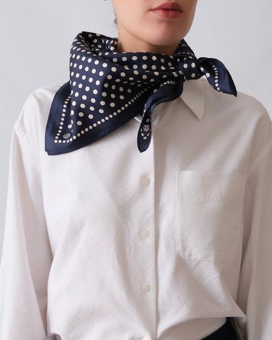 Person wearing a navy blue scarf with white polka dots over a white shirt against a light gray background