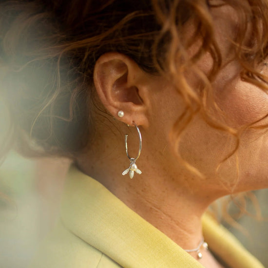 Large silver hoop earrings with flying bee pendants and a rice pearl drop with butterfly earring fastenings