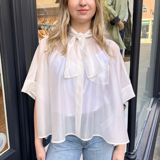 Woman wearing a white blouse with a bow tie in front with blue jeans.