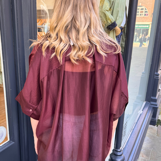 Women wearing burgundy sheer blouse with tie neck and blue jeans.