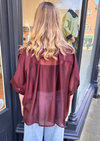 Women wearing burgundy sheer blouse with tie neck and blue jeans.