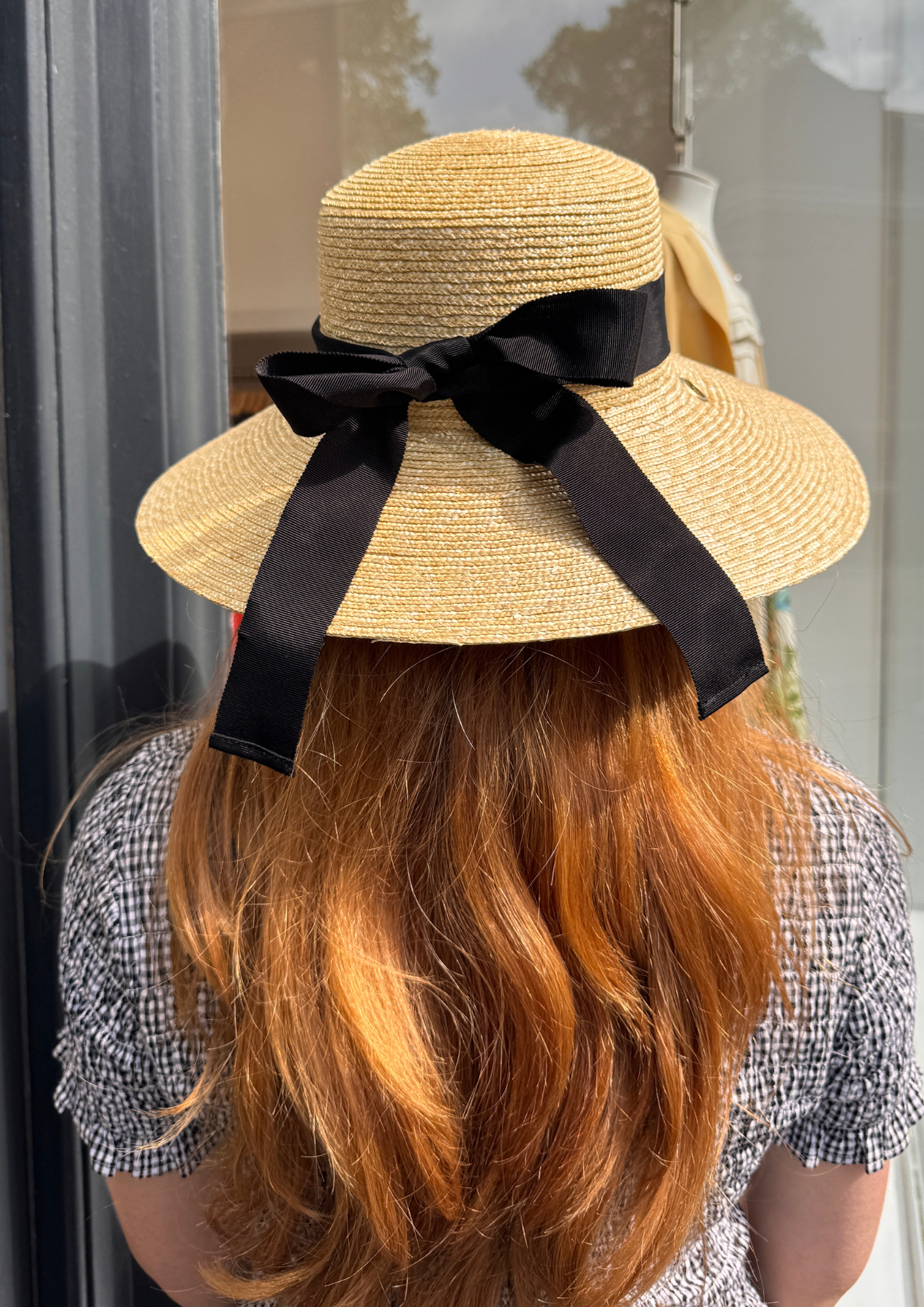 Person wearing a straw hat with a black ribbon tied in bow in the back