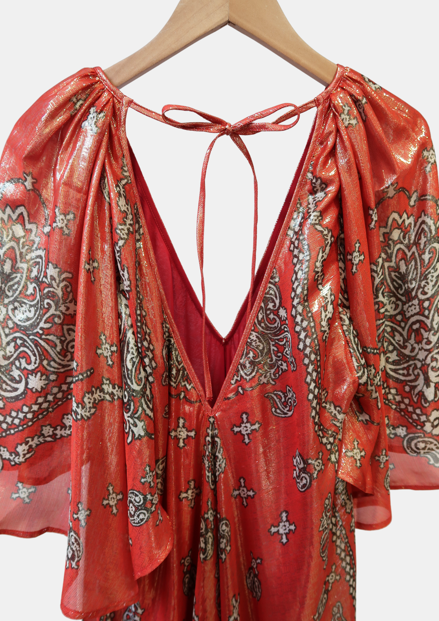 Red and gold patterned dress on a hanger against a white background