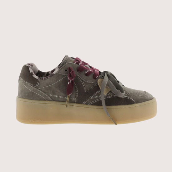A low-top platform sneaker in dark gray suede and leather, featuring a thick beige gum sole, gray laces, and burgundy ribbon laces tied in a bow.