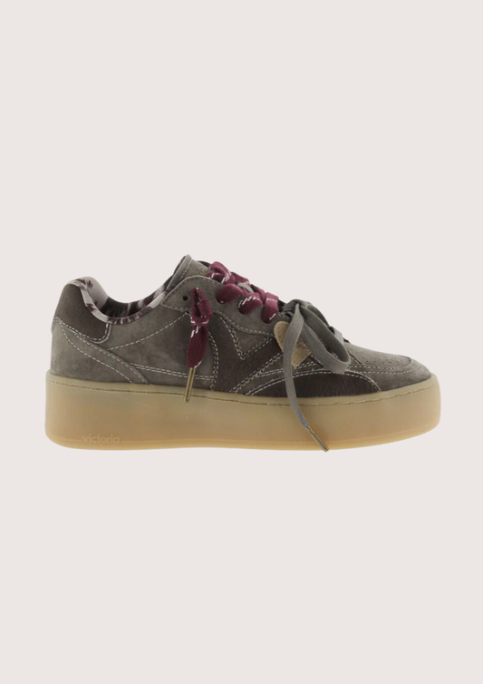 A low-top platform sneaker in dark gray suede and leather, featuring a thick beige gum sole, gray laces, and burgundy ribbon laces tied in a bow.