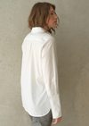 White button up shirt with a curved hem and wide collar, with three buttons  at the neck.  Back view. 