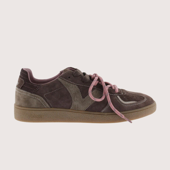 A low-top sneaker in dark brown suede and gray fabric panels, featuring dusty pink laces and a tan rubber sole, shown against a light beige background.