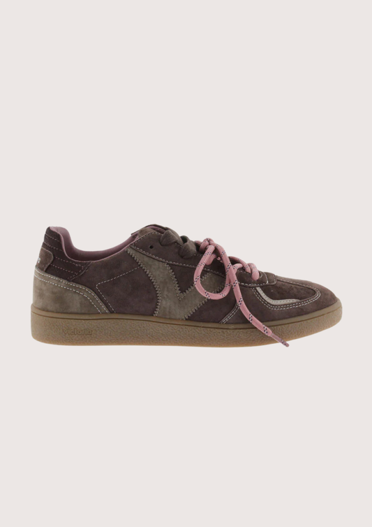 A low-top sneaker in dark brown suede and gray fabric panels, featuring dusty pink laces and a tan rubber sole, shown against a light beige background.