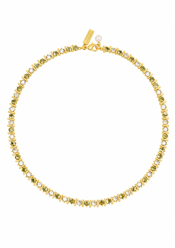 A gold tennis necklace featuring small green gemstones and clear stones, displayed on a clean white background. A gold tag is attached near the clasp.