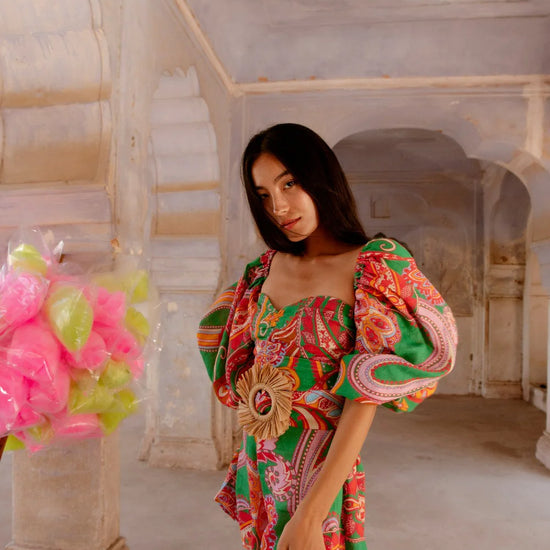 Green red and pink paisley print playsuit with oversized puff sleeves and a circle raffia belt