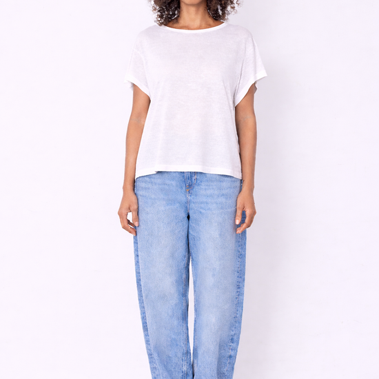 model wearing white top and jeans on plain background 