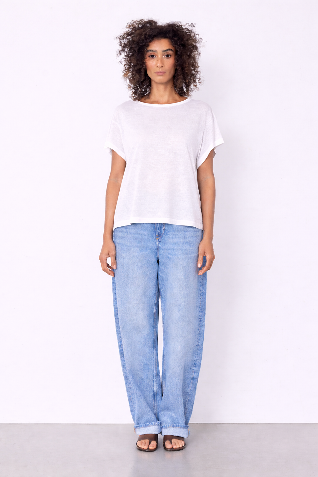 model wearing white top and jeans on plain background 
