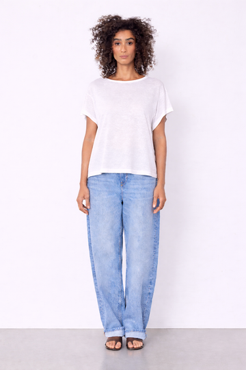 model wearing white top and jeans on plain background 